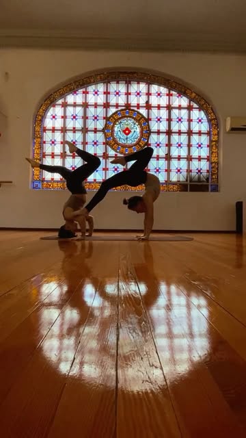 Dos alumnxs de FLEXUP practicando parada de manos frente al vitral de la sala, en Montevideo — foto real de @flexup.uy